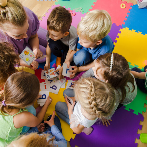 Group of kindergarten kids sitting closely on a floor together with teacher, providing group work. Children learning to cooperate while solving tasks.