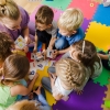 Group of kindergarten kids sitting closely on a floor together with teacher, providing group work. Children learning to cooperate while solving tasks.