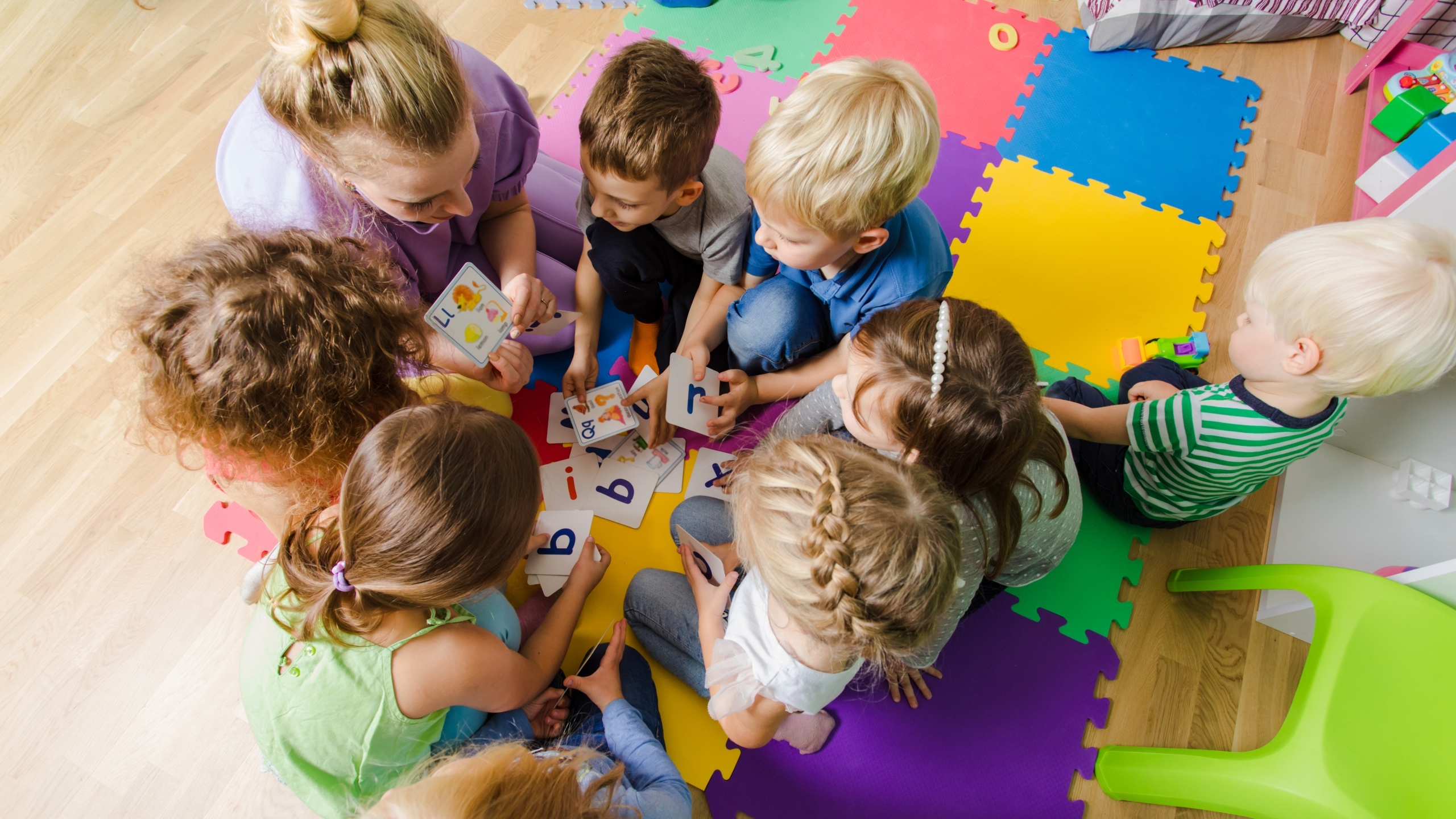 Group of kindergarten kids sitting closely on a floor together with teacher, providing group work. Children learning to cooperate while solving tasks.
