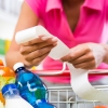 Unrecognizable woman checking a long grocery receipt leaning to a full shopping cart at store.