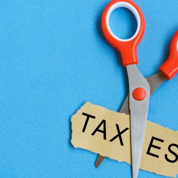 Scissor cutting the word 'taxes' in a piece of paper.