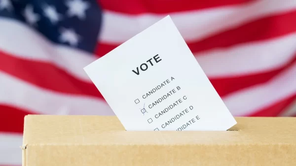 voting and civil rights concept - vote inserted into ballot box slot on election over american flag