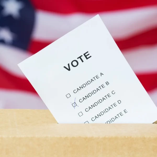 voting and civil rights concept - vote inserted into ballot box slot on election over american flag