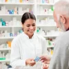 Medicine, pharmaceutics, health care and people concept - happy pharmacist giving medications to senior man customer