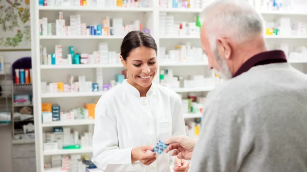 Medicine, pharmaceutics, health care and people concept - happy pharmacist giving medications to senior man customer