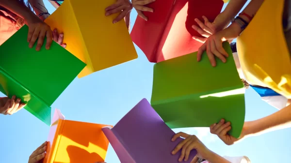 School children read books outdoors and learn about nature. Group of students standing in circle and holding red, green, yellow, orange and purple books in hands. Low angle bottom view shot from below