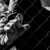 Young unidentifiable teenage boy holding the wired garden at the correctional institute in black and white, conceptual image of juvenile delinquency, focus on the boys hand.
