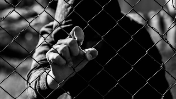 Young unidentifiable teenage boy holding the wired garden at the correctional institute in black and white, conceptual image of juvenile delinquency, focus on the boys hand.