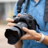 Young male photographer with camera outdoors, closeup