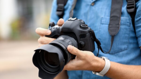 Young male photographer with camera outdoors, closeup